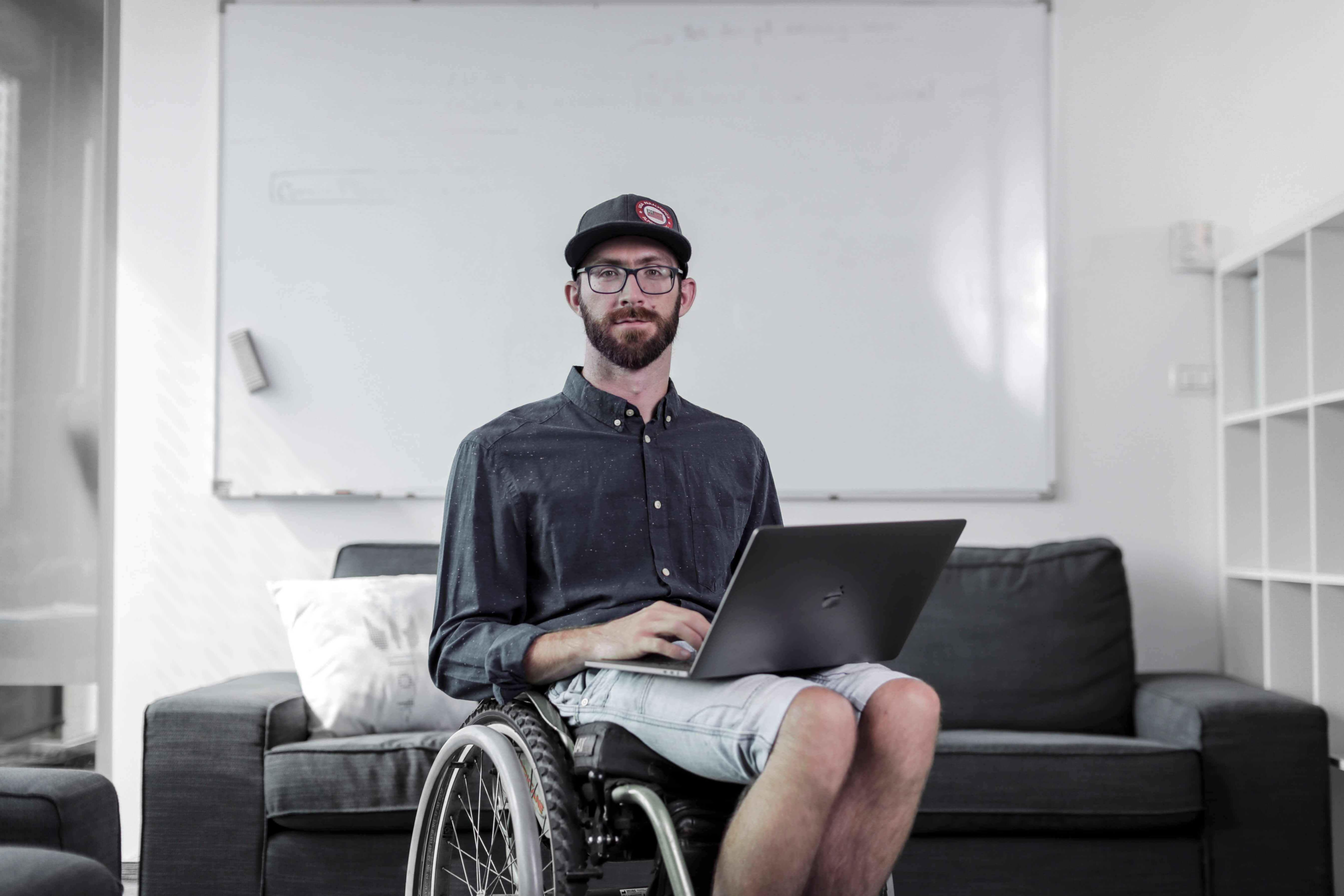 Gal Jakic sitting on a wheelchair, holding a laptop in his lap, looking at the camera. © Aljoša Rebolj